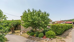 Entorno rural con un muro de piedra, un camino bordeado de árboles y edificios tradicionales con tejados rojos.