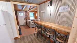 Eine kleine Küche mit einer Holztresen-Bar, einem Kühlschrank und einem Schild, das den Weg zum See weist.