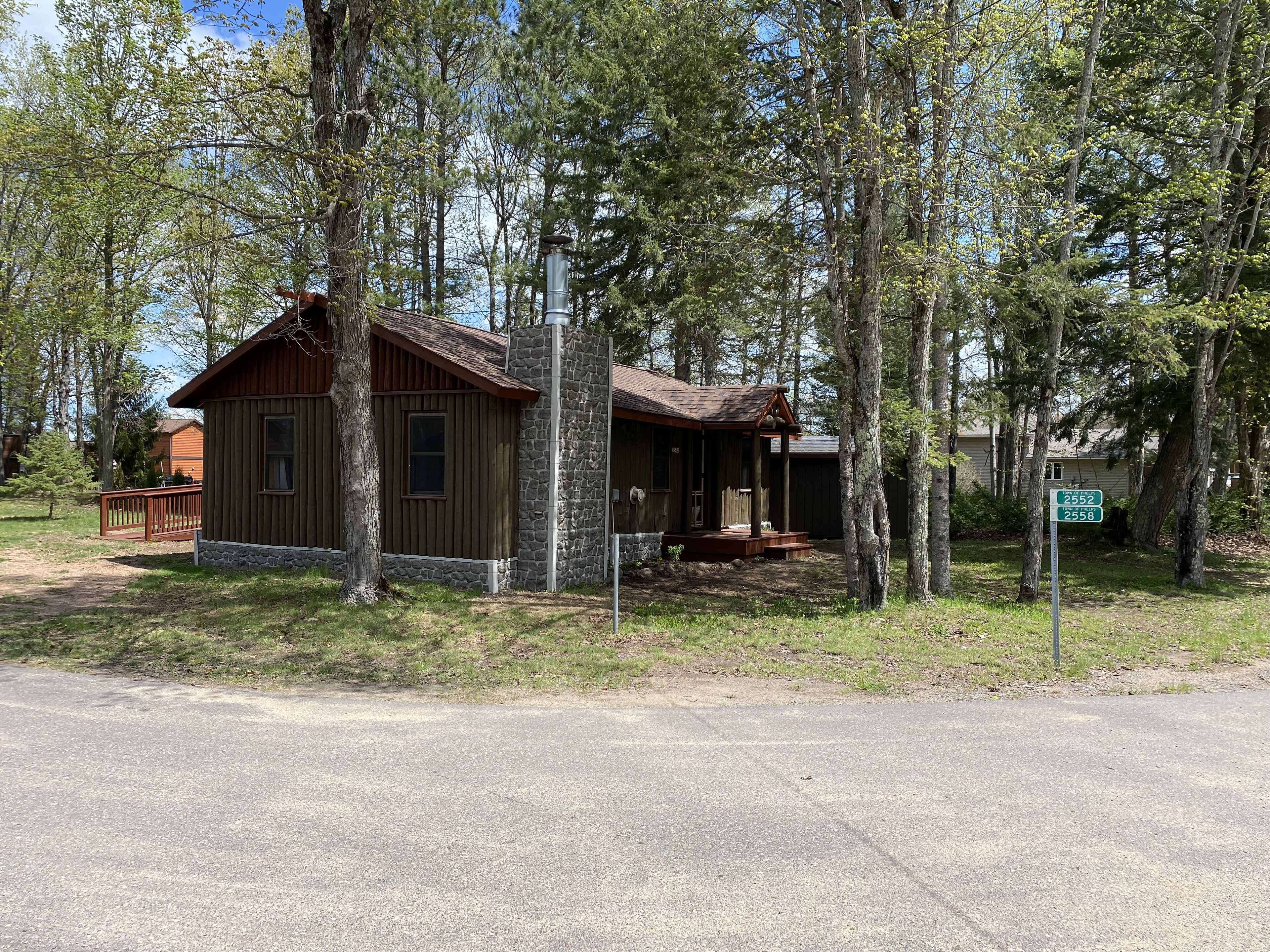 Une cabane rustique, dotée de fondations en pierre et d’un revêtement extérieur en bois, entourée de grands arbres.