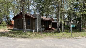 Une cabane rustique, dotée de fondations en pierre et d’un revêtement extérieur en bois, entourée de grands arbres.
