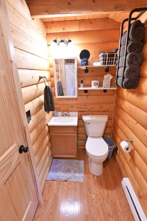 Ein kleines Badezimmer in einer Holzhütte mit Waschbecken, Toilette und Spiegel.