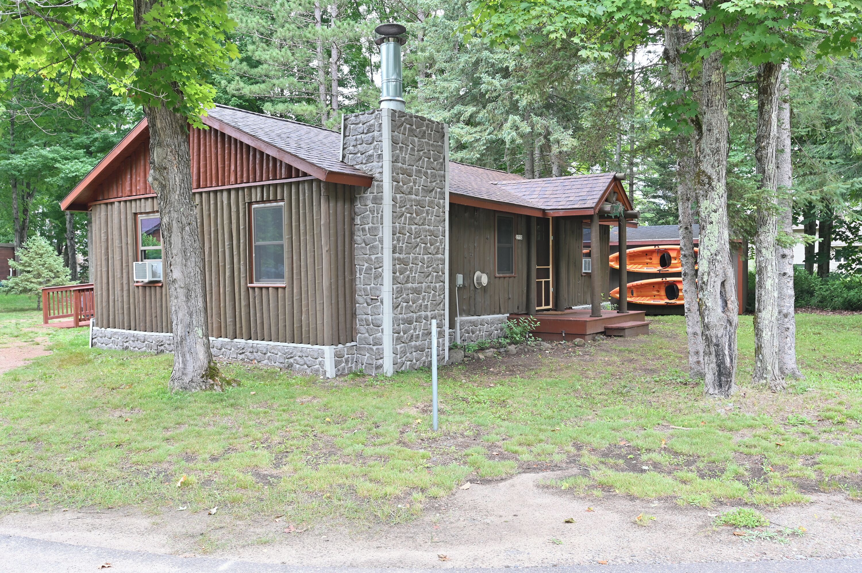 A cabin with a stone exterior, wooden deck, and a chimney.