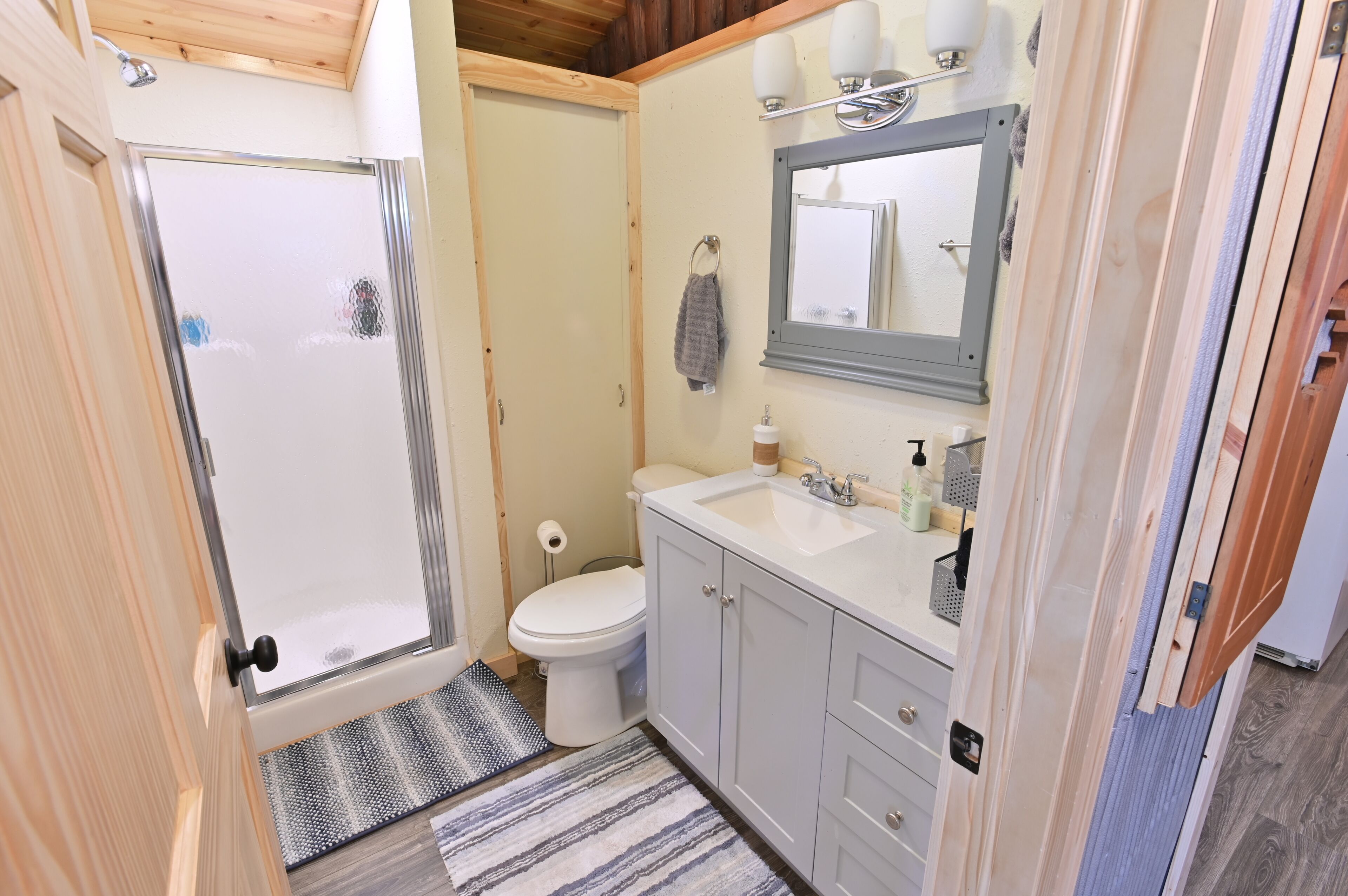 A bathroom with a shower, toilet, sink, and mirror.