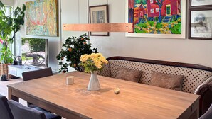 Un coin repas avec une table en bois, un vase rempli de fleurs, un banc à motifs à pois et des œuvres d’art accrochées aux murs.