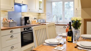 A modern kitchen with white cabinets, a built-in oven, a coffee maker, and a dining area with a table set for two. - 2 bedroom accommodation in Tregaron, near Lampeter (Tregaron, near Lampeter)
