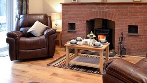 A cozy living room with a brick fireplace, leather armchair, and a table set for tea. - 2 bedroom accommodation in Tregaron, near Lampeter (Tregaron, near Lampeter)