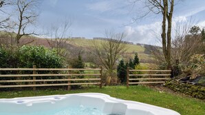 A hot tub in a garden with a wooden fence and hills in the background. - 2 bedroom accommodation in Tregaron, near Lampeter (Tregaron, near Lampeter)