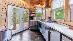 A modern kitchen with wooden walls, a stainless steel refrigerator, and a large window with blinds.