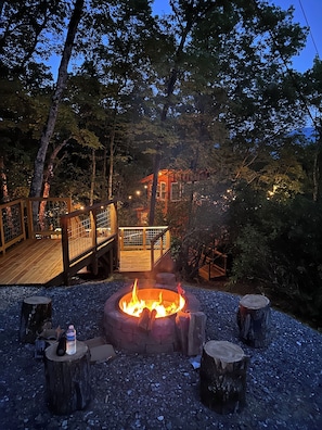 A fire pit surrounded by wooden stumps, a wooden deck, and a metal railing. - Tree House Cabin w Hot tub close to downtown & Great Smoky Mountains (Bryson City)