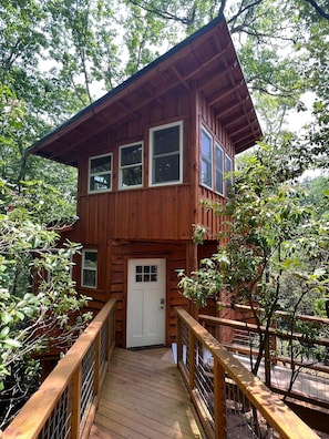 A two-story wooden cabin with a wooden deck and a white door. - Tree House Cabin w Hot tub close to downtown & Great Smoky Mountains (Bryson City)