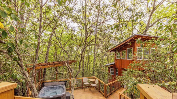 A wooden deck with a hot tub and seating area surrounded by trees.