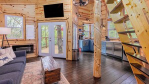 A wooden cabin interior with a living room, kitchen, and a staircase.
