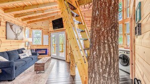 A log cabin interior with a wooden staircase, a sofa, a rug, and a washing machine.