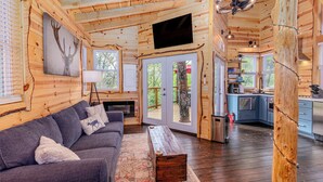 A log cabin interior with a sofa, a coffee table, a fireplace, a television, and a kitchen area.