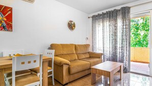 A living room with a sofa, a coffee table, a dining table with chairs, and a painting on the wall. - Nice apartment in Almuñécar with WiFi (Almuñécar)