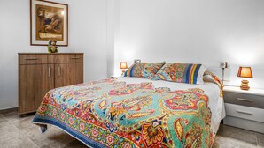 A bedroom with a colorful bedspread, a wooden wardrobe, a framed picture on the wall, and bedside lamps. - Nice apartment in Almuñécar with WiFi (Almuñécar)
