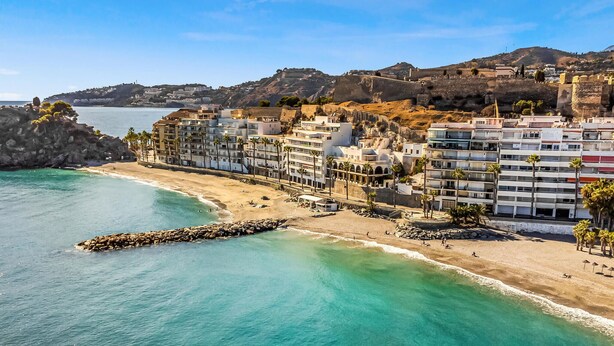 A coastal hotel with multiple floors, a beach in the foreground, and a rocky hillside in the background. - Nice apartment in Almuñécar with WiFi (Almuñécar)