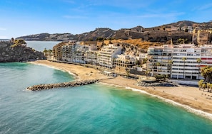 A coastal hotel with multiple floors, a beach in the foreground, and a rocky hillside in the background. - Nice apartment in Almuñécar with WiFi (Almuñécar)