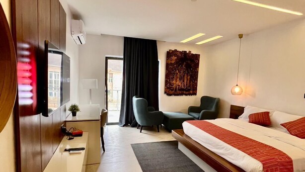 A modern hotel room with a large bed, a desk, a chair, and a TV mounted on the wall. - Luxor Apartments (Asaba)