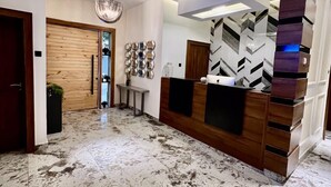 A modern reception area with a marble floor, wooden paneling, and a geometric wall design. - Luxor Apartments (Asaba)