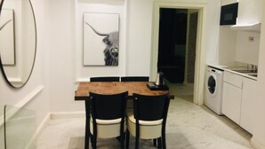 A compact kitchen with a washing machine, a dining area with a wooden table and chairs, and a framed artwork on the wall. - Luxor Apartments (Asaba)