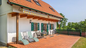 A house with a tiled roof, green shutters, and a covered patio with outdoor furniture.
