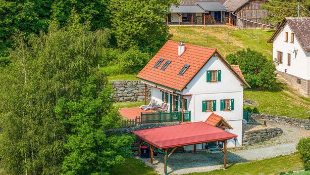 A two-story house with a red roof, a covered porch, and a stone wall.
