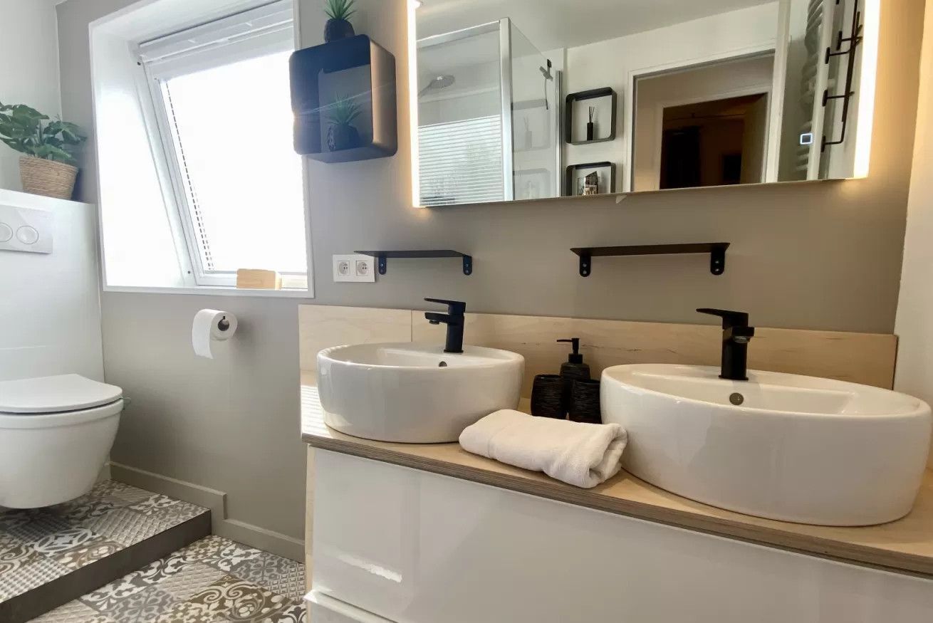 A modern bathroom with two sinks, a toilet, a window, and a mirror.