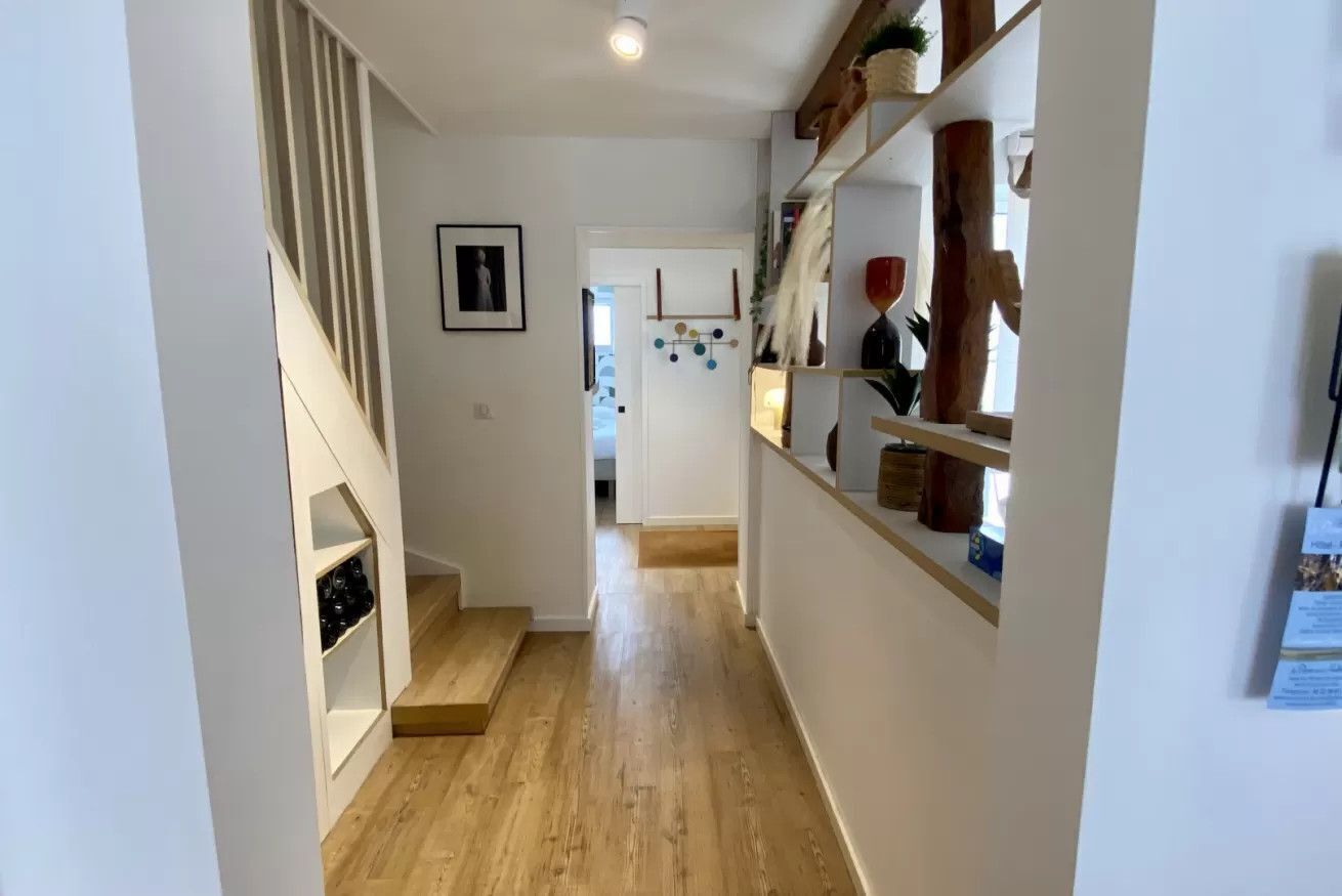 A hallway with wooden flooring, white walls, a staircase, and shelves with various items.