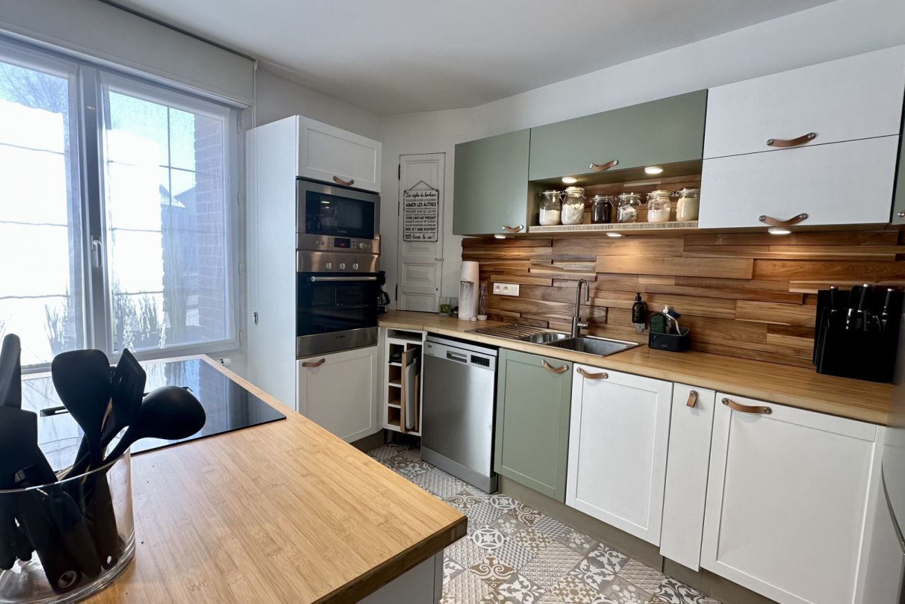 Une cuisine moderne dotée d’un plan de travail en bois, d’appareils électroménagers en acier inoxydable et d’une fenêtre.