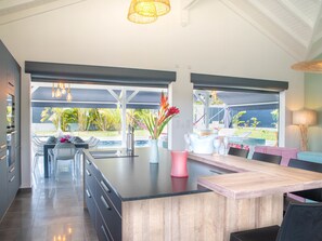Eine moderne Küche mit Kochinsel, Essbereich und großen Fenstern mit Blick auf einen Pool und Garten.