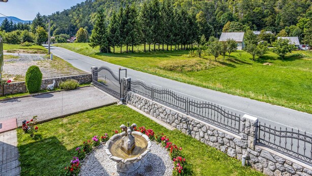 A paved road with a stone wall and metal fence, surrounded by greenery and houses. - Amazing home in Lic with WiFi (Lic)