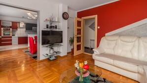 A modern living room with a TV, a glass coffee table with flowers, a white leather sofa, and a red accent wall. - Amazing home in Lic with WiFi (Lic)