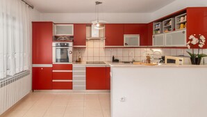 A compact kitchen with red cabinetry, a built-in oven, and a central island with a sink and countertop. - Amazing home in Lic with WiFi (Lic)