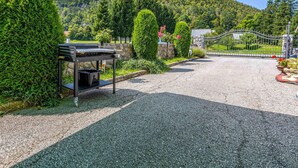 A gravel driveway leading to a gated entrance with a barbecue grill and neatly trimmed hedges. - Amazing home in Lic with WiFi (Lic)