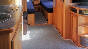 Ein kompaktes Wohnmobil-Interieur mit Küchenzeile, einem Bett, einem Fernseher und einer kleinen Sitzecke.