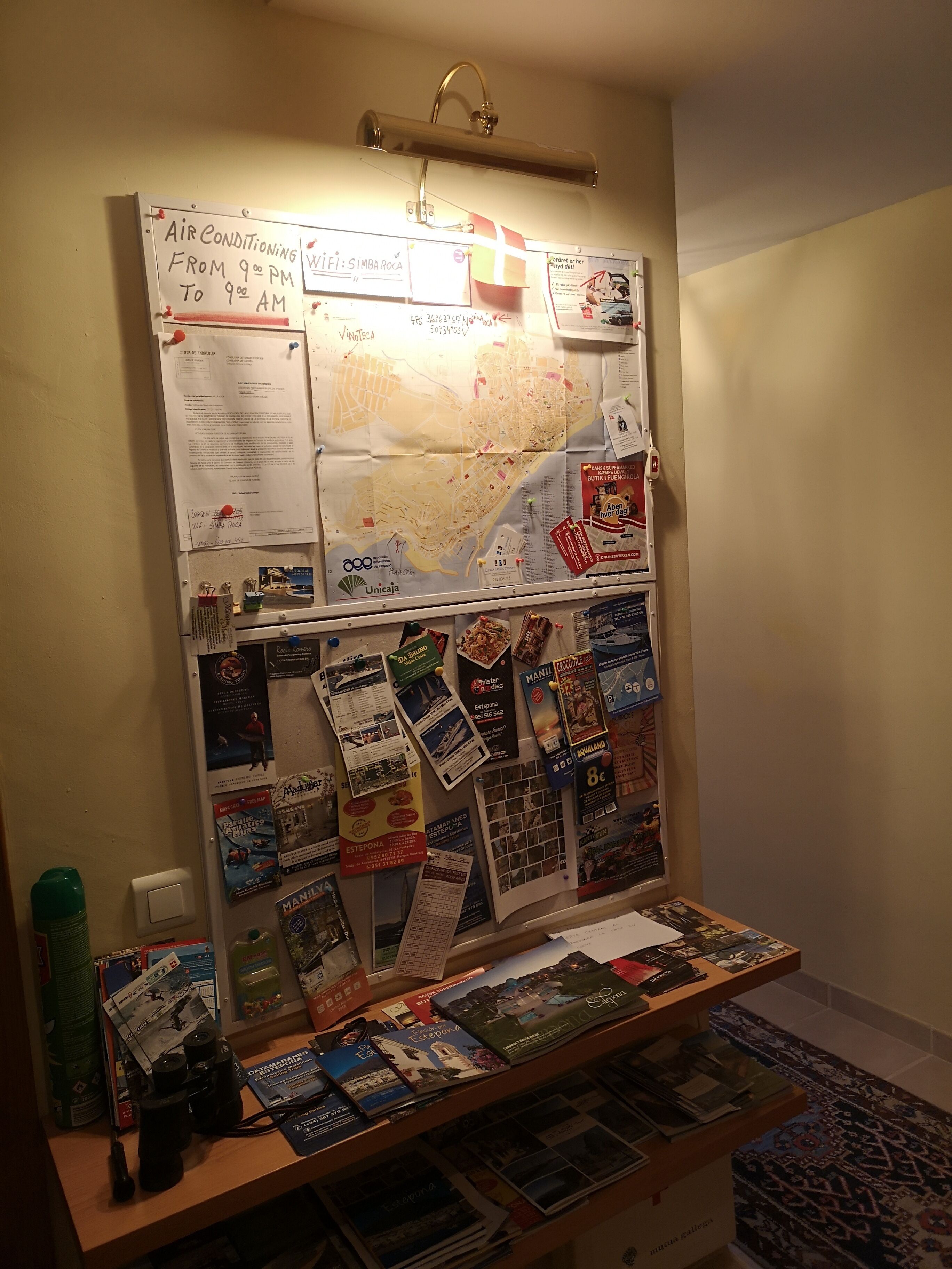 A bulletin board with various travel brochures, a map, and a sign indicating air conditioning hours.