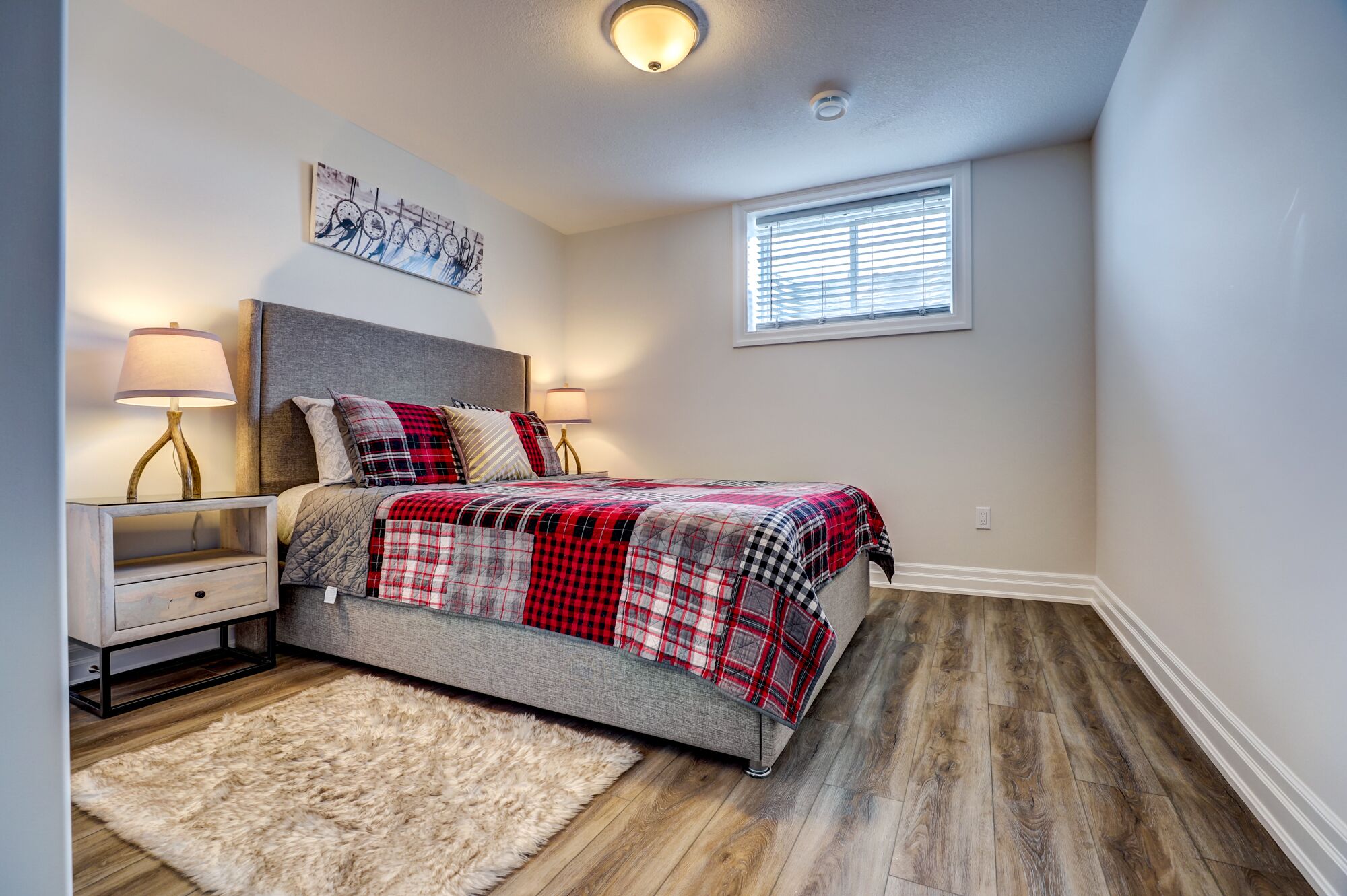 A bedroom with a bed, a nightstand, a lamp, a fluffy rug, a window, and a ceiling light.
