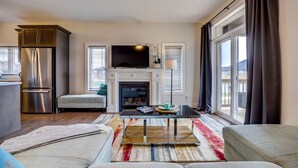 Una sala de estar moderna con chimenea, televisor, sofá y comedor con refrigerador.
