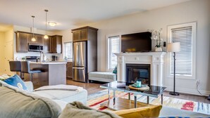 Una sala de estar moderna con chimenea, una cocina con electrodomésticos de acero inoxidable y un comedor.