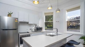 Una cocina moderna con un refrigerador de acero inoxidable, un horno empotrado, un microondas y un lavamanos. Hay luces colgantes sobre la encimera y una ventana con vistas al exterior.