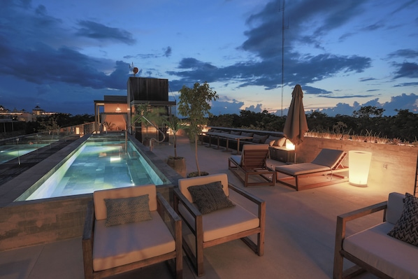 Zona de piscina en la azotea con sillones reclinables y un bar.