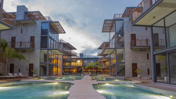 A modern hotel with a central pool, multiple balconies, and a contemporary architectural design. - Luxury Condos Tulum - Private Cenote (Tulum)