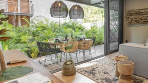 A modern outdoor dining area with wicker chairs and a wooden table, surrounded by lush greenery and a patterned rug. - Luxury Condos Tulum - Private Cenote (Tulum)