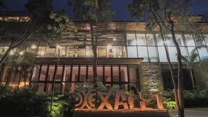 A modern building with a large illuminated sign reading "DEKALB" in the foreground, surrounded by lush greenery and trees. - Luxury Condos Tulum - Private Cenote (Tulum)