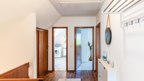 A hallway with a wooden staircase, a rug, a white wall with a painting, and a door leading to a laundry room. - Lovely apartment in Hasselberg with WiFi (Hasselberg)