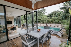 Un espace repas extérieur moderne avec une piscine, entouré d’une végétation luxuriante.