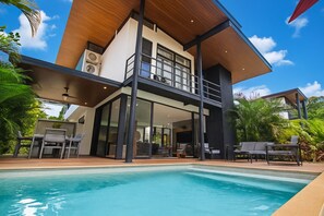 A modern two-story house with a swimming pool, large windows, and outdoor furniture.