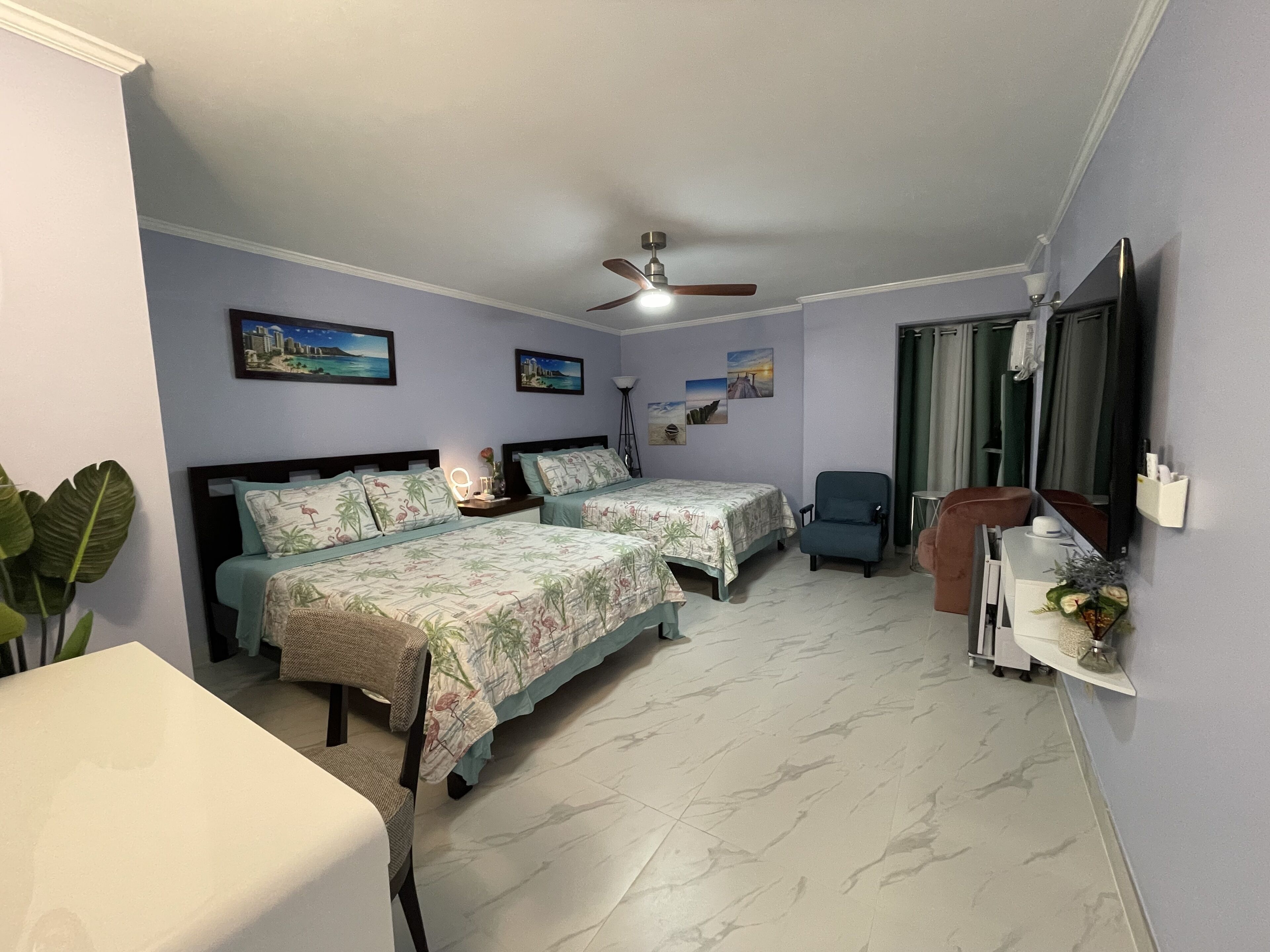 A bedroom with two beds, a ceiling fan, a TV, and a small table with a vase.