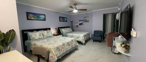 A bedroom with two beds, a ceiling fan, a TV, and a small table with a vase.